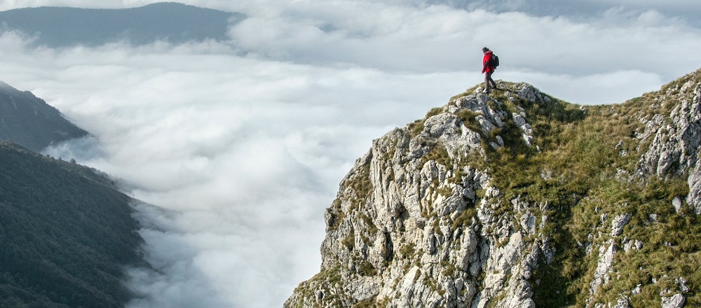 Photo of a hiker on the summit of a rocky peak, looking out over a majestic valley