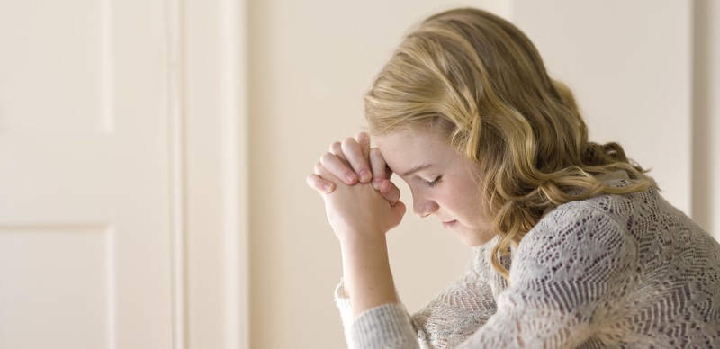 Photo of a young woman kneeling by her bed and praying